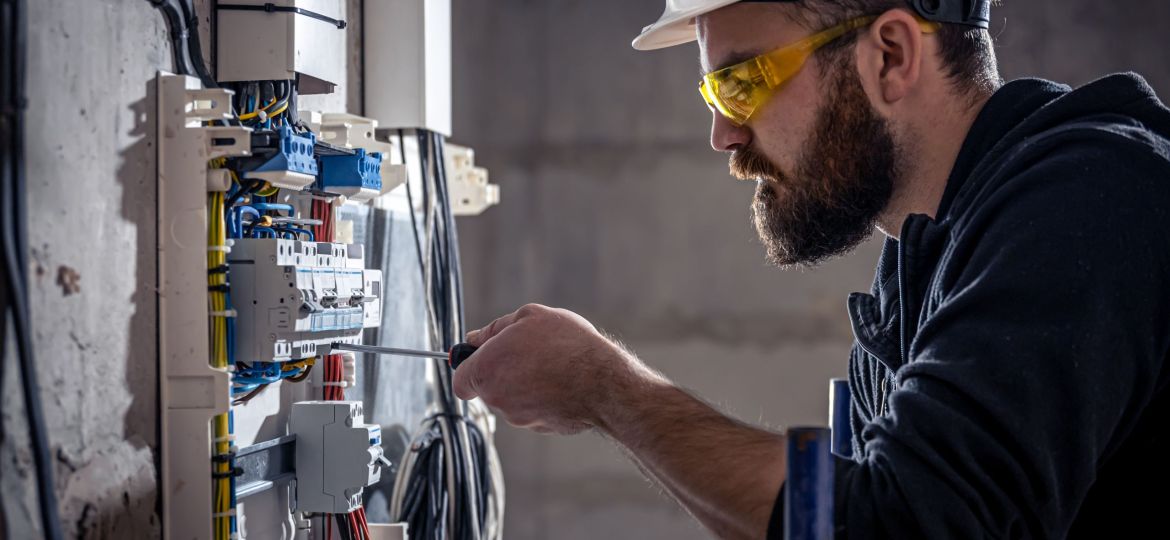 A male electrician works in a switchboard with an electrical connecting cable.